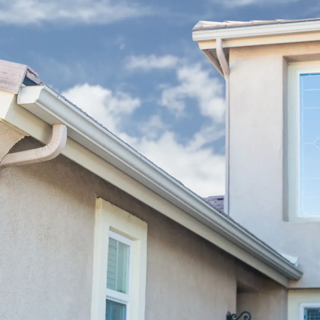 White seamless gutter and downspout along the roofline of a stucco home under a blue sky