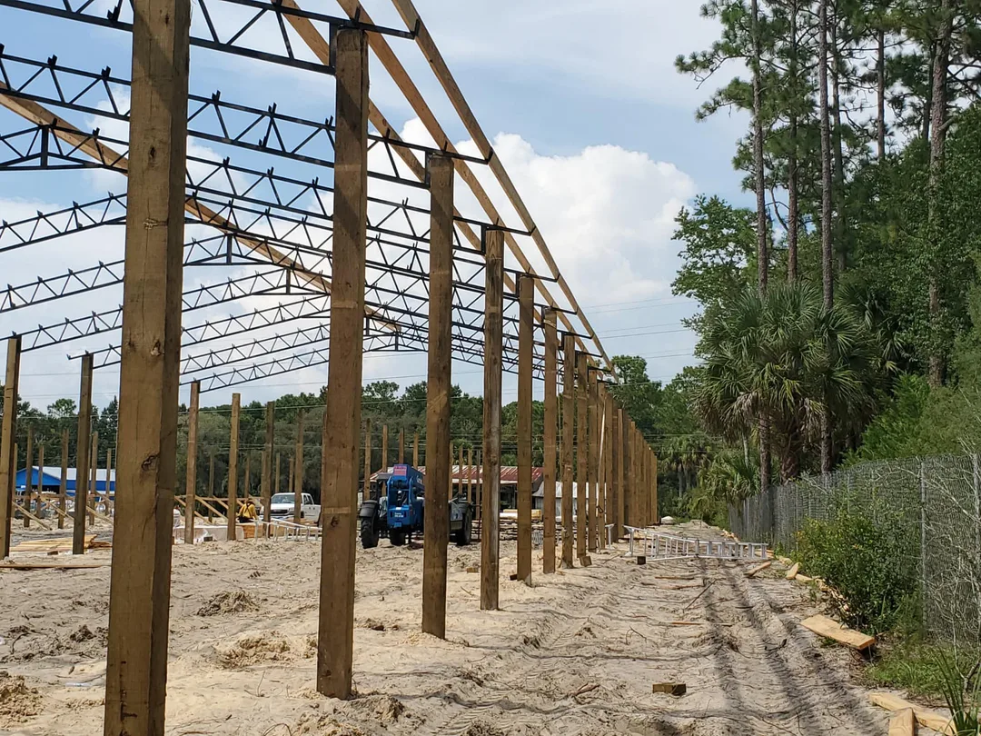 Pole barn wood post and steel truss frame under construction along a wooded property line